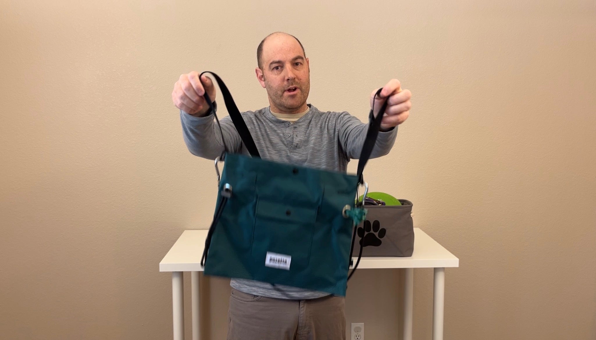 Load video: Brandon, founder of Puzette Bagworks, demonstrates the features of the Puzette dog walking bag, including the front poop bag dispenser, snap-close treat pocket, and cinch cord. He then shows how the Puzette holds a water bottle, water bowl, toys, leash and other gear. He then demonstrates the stabilizer cord which keeps the bag from sliding when he bends over. The bag is shown in an indoor setting.