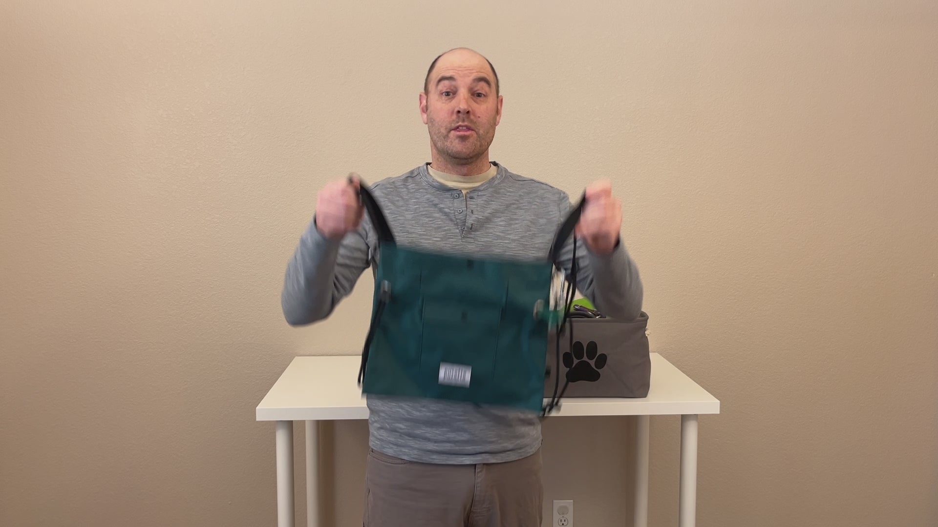 Load video: Brandon, founder of Puzette Bagworks, demonstrates the features of the Puzette dog walking bag, including the front poop bag dispenser, snap-close treat pocket, and cinch cord. He then shows how the Puzette holds a water bottle, water bowl, toys, leash and other gear. He then demonstrates the stabilizer cord which keeps the bag from sliding when he bends over. The bag is shown in an indoor setting.